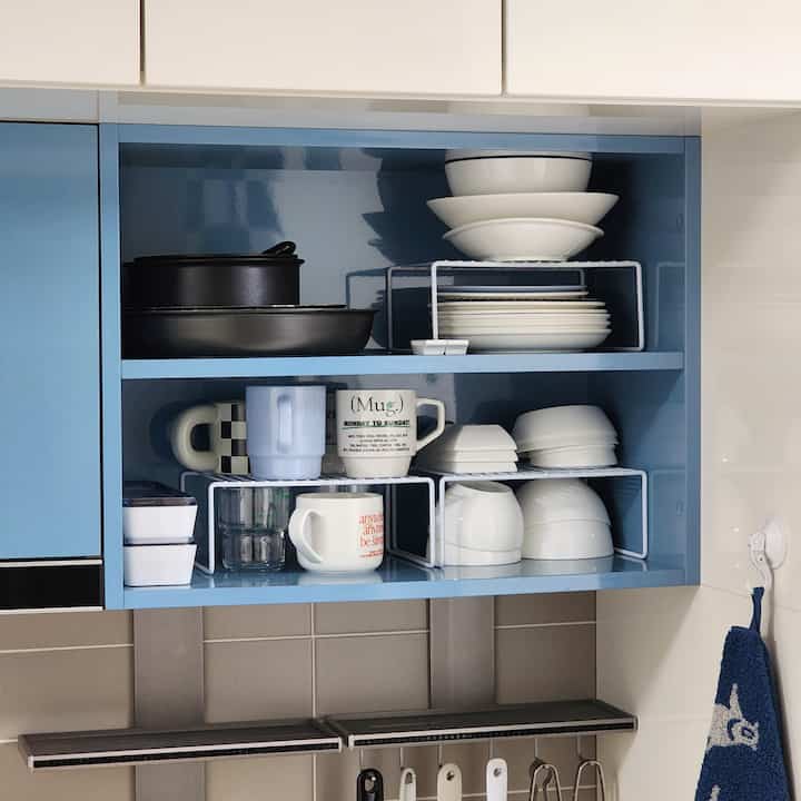 Blue kitchen cabinet interior featuring neatly organized white dishes and mugs with efficient storage ideas