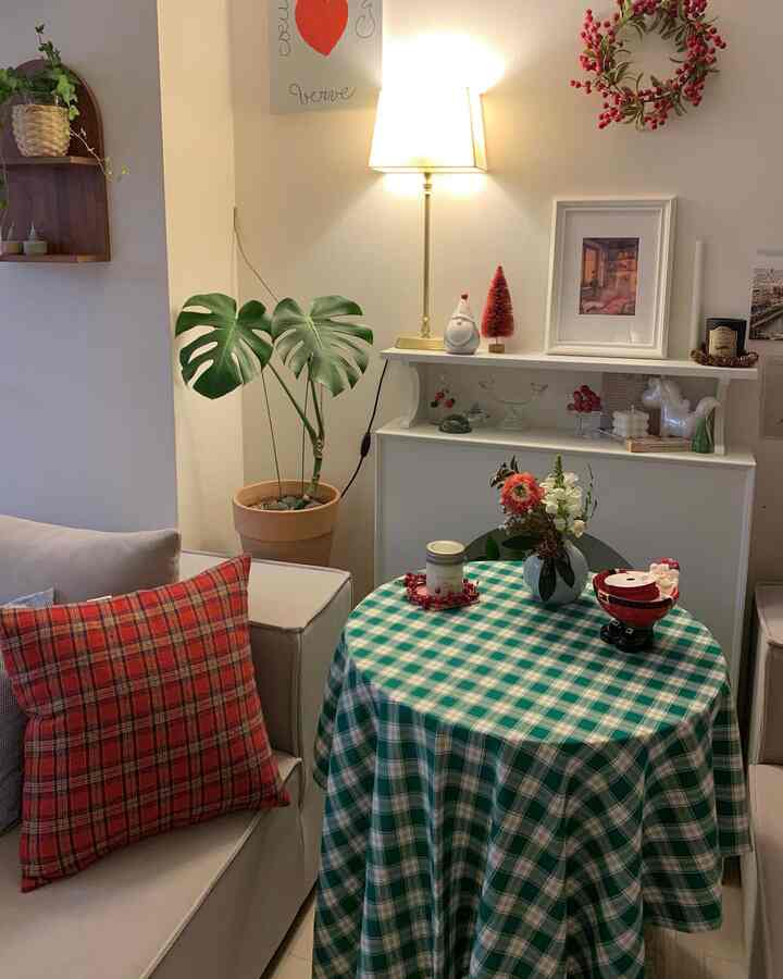 Cozy living room with warm lighting and Christmas decorations, featuring a red check cushion and green check tablecloth as focal points