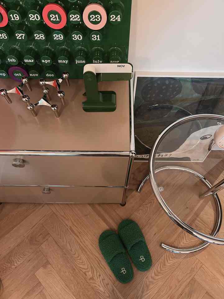 ベージュの壁と木の床の空間にクロームフレームの家具と緑のスリッパが置かれたナチュラルモダンなインテリア