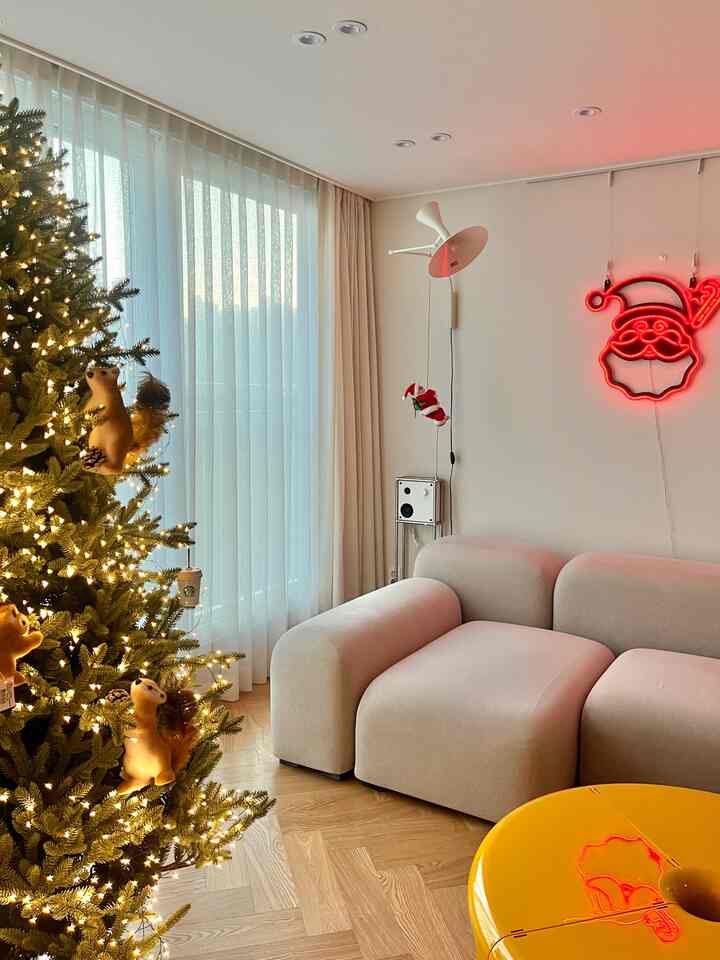 Bright white and wood tone living room featuring a decorated Christmas tree and neon Santa sign with a modern atmosphere