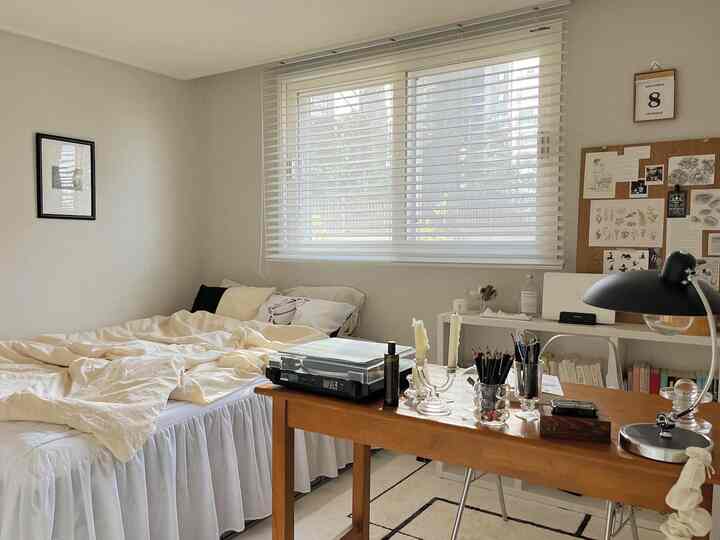 White and beige toned bedroom featuring a wooden desk and bookshelf in a cozy home office space
