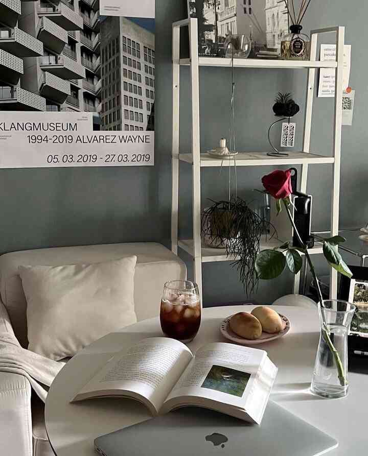 White and gray toned studio living room featuring a cozy single sofa and round table with book and iced coffee creating a warm atmosphere