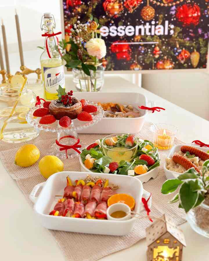 White dining table set for a Christmas home party featuring red ribbons, various dishes, and a warm candlelight ambiance