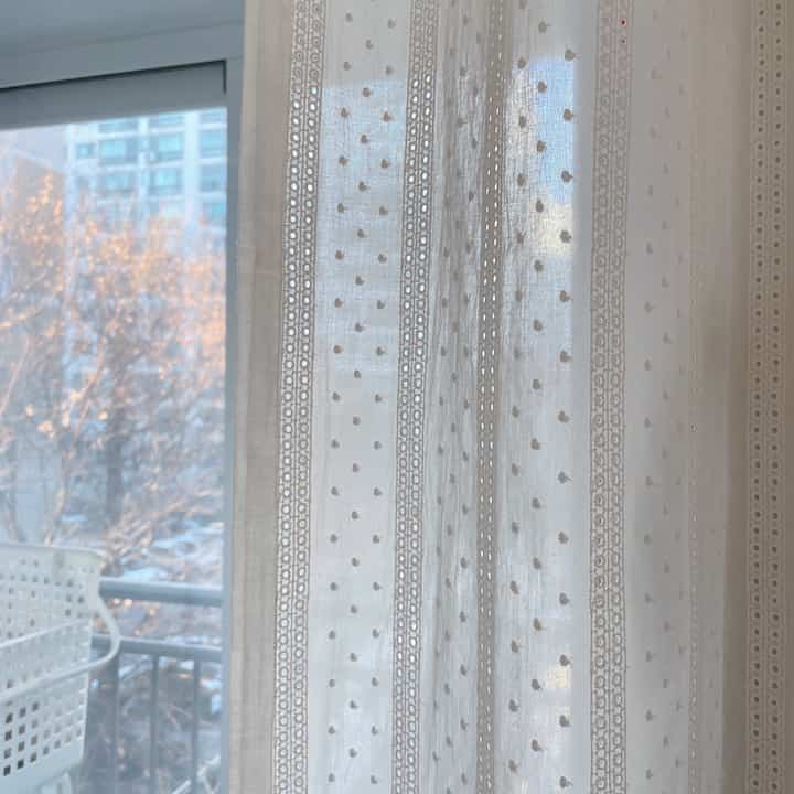A bright white-tone space featuring transparent lace curtains in front of a balcony, allowing soft natural light to filter in