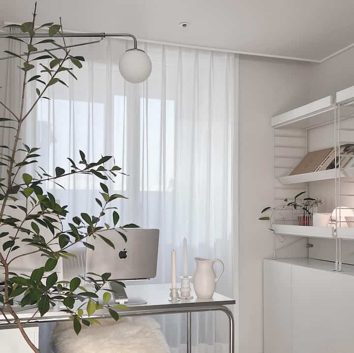 White-toned home office featuring a desk with a laptop and plants, showcasing a clean modern interior