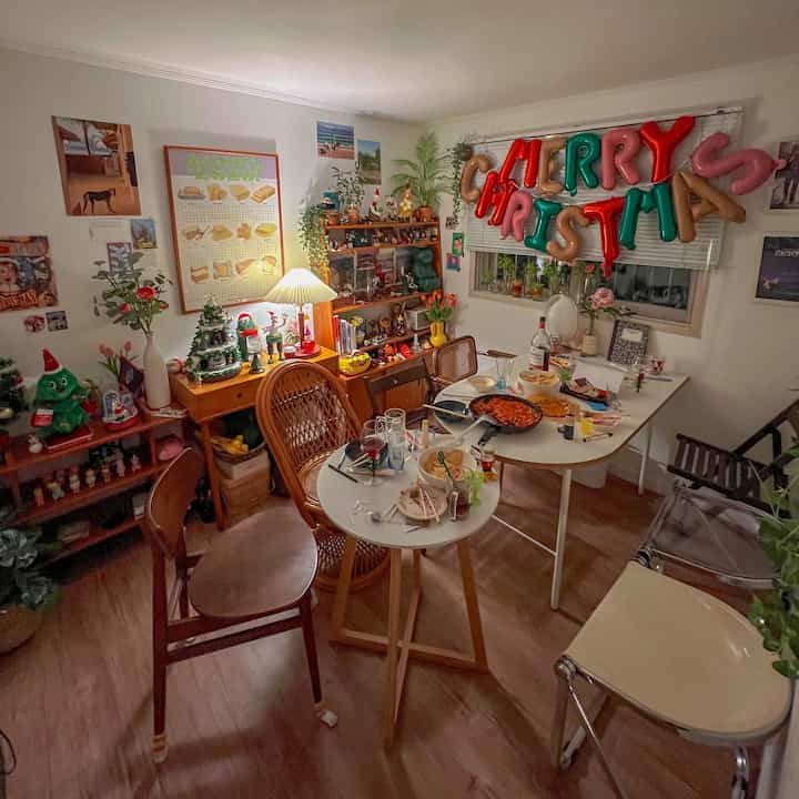 Cozy dining room with white walls and wood floor, red and green Christmas balloons, vintage decor, assorted chairs capturing a home party atmosphere