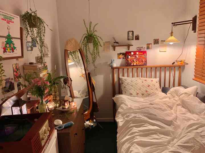 Cozy studio bedroom featuring warm wood tones, vintage decorations, white bedding, and green plants creating a relaxed atmosphere
