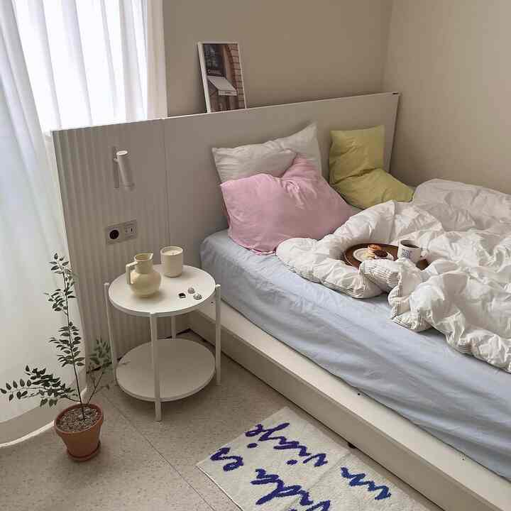 Soft white and pastel-toned bedroom featuring a white bed, side table, and a natural plant creating a cozy atmosphere