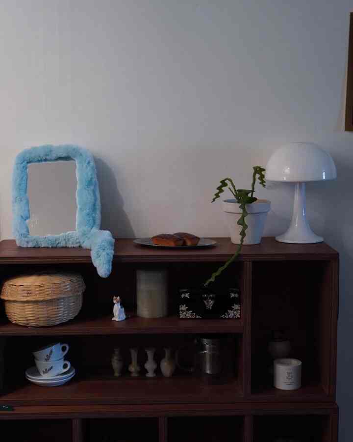 ブラウンのウッドトーンキャビネットとホワイトの小物、ブルーのファーフレームミラーが配置された落ち着いた室内