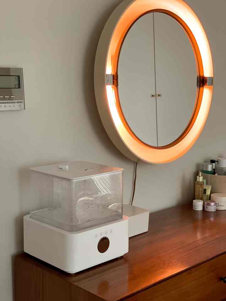 White and wood-toned bedroom vanity featuring a vintage mirror and humidifier, creating a cozy and warm atmosphere