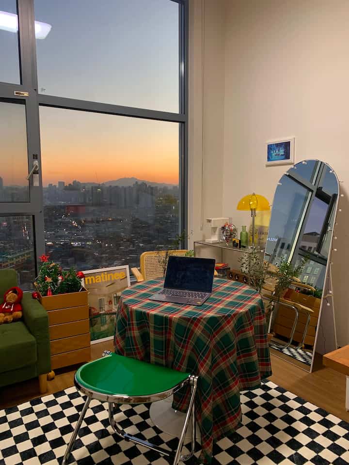 緑のチェック柄テーブルクロスがあるワンルーム、夕焼けの背景とクリスマス装飾が調和した温かみのあるインテリア