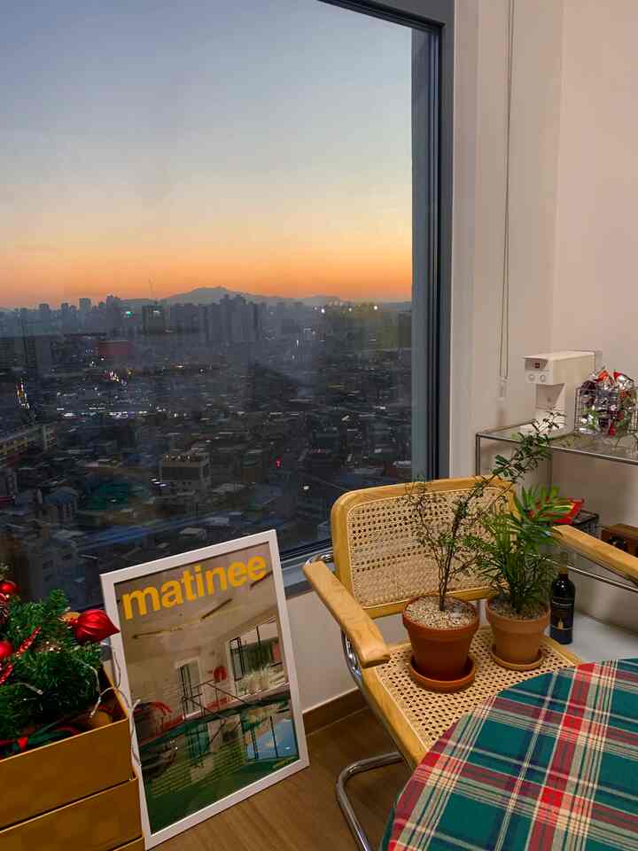 Cozy home cafe corner with wood tone armchair, plaid tablecloth, beside a window showing sunset hues
