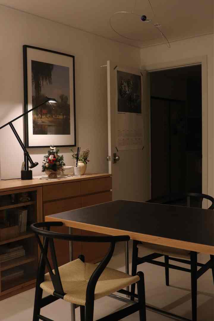 A calm two-person dining room in black and wood tones featuring an Artemide Tizio table lamp and wooden cabinet