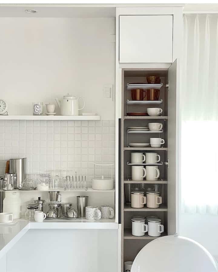 白とナチュラルトーンのキッチン、整然と収納されたマグカップとキッチン用品が配された清潔感のあるインテリア