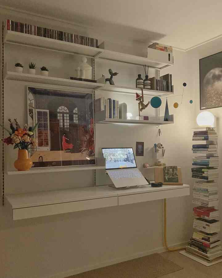 A modern study with white and beige tones featuring a floating desk and bookshelf arranged in a neat layout