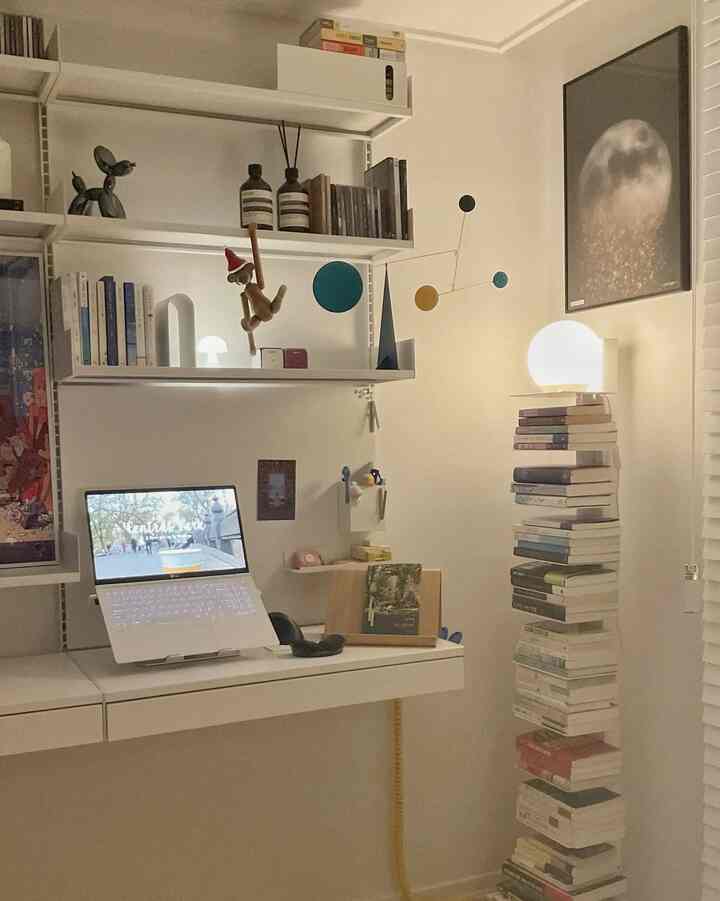 White and beige-toned home office space featuring desk, shelves with books, and decorative objets in a simple modern style