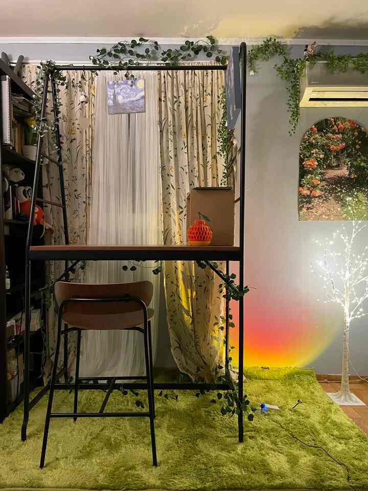 A cozy small home office with a green rug and plant decorations, featuring a desk and curtains