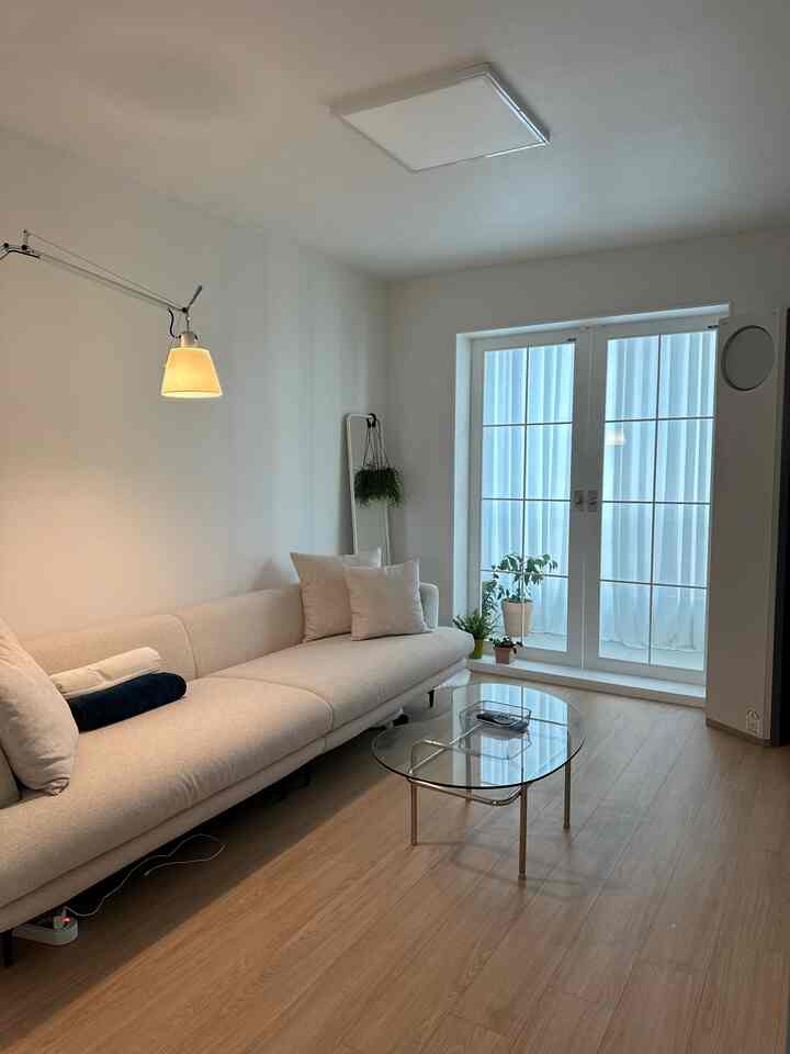 Bright white and natural-toned living room featuring a beige sofa and glass coffee table in a modern setting