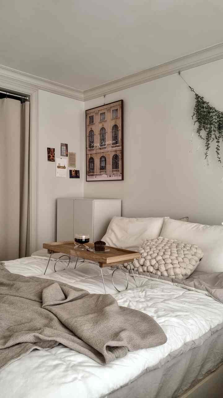 White and beige toned bedroom featuring wooden tray and cozy accents with a warm, simple atmosphere