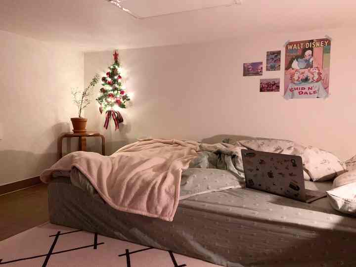 A pink and natural toned bedroom featuring a wall-mounted Christmas tree and Disney posters with cozy decor
