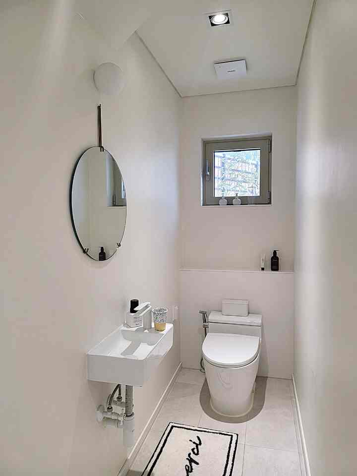 明るいホワイトトーンの狭いミニマルなトイレ、壁掛け鏡と小さな洗面台、便器が配置されたすっきりとした空間