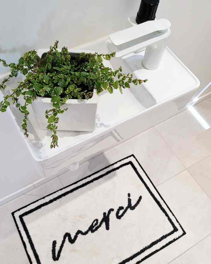 Minimal white and beige mini bathroom featuring a compact sink and green plant with a simple modern vibe
