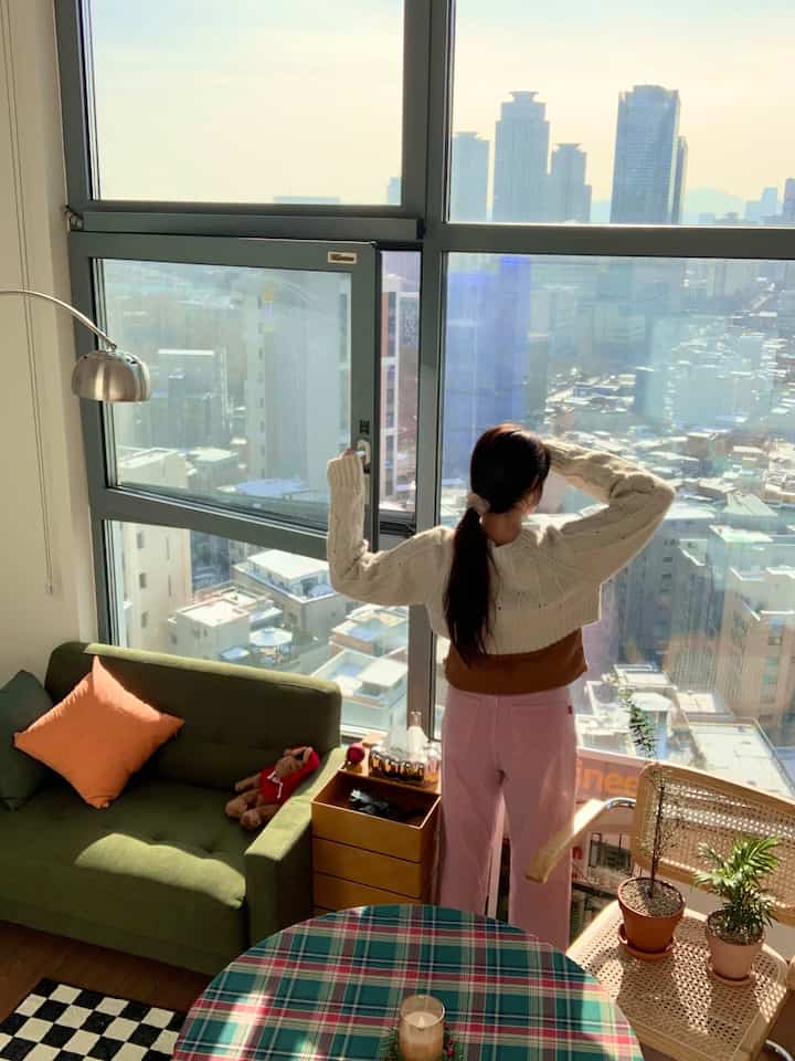 Natural-toned studio apartment living room featuring a comfortable sofa, dining table, and large windows with city view, creating a cozy atmosphere