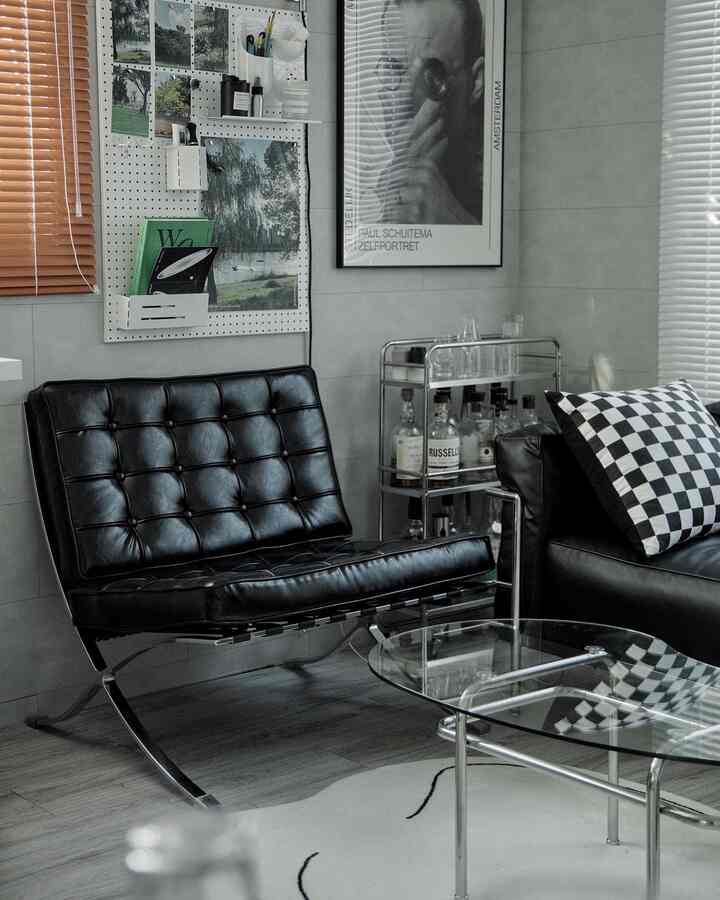 Modern living room with gray walls and flooring featuring black leather sofa and armchair