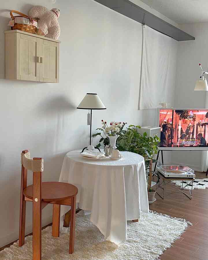 白と木目調が調和したワンルームのリビング、テーブルや植物、照明が配置されたシンプルでモダンな雰囲気のあるインテリア