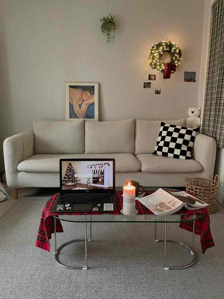 Nordic-style living room with cream sofa and glass table featuring red plaid table runner, decorated in Christmas mood