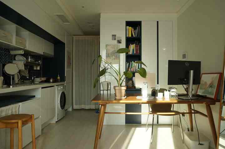 White and navy toned studio apartment home office, featuring practical dining table and computer desk with natural ambiance