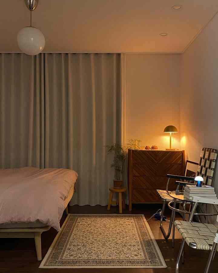 Cozy bedroom with warm wood tones and soft pink bedding, featuring a Persian rug, curtains, and ambient lighting creating a snug atmosphere.