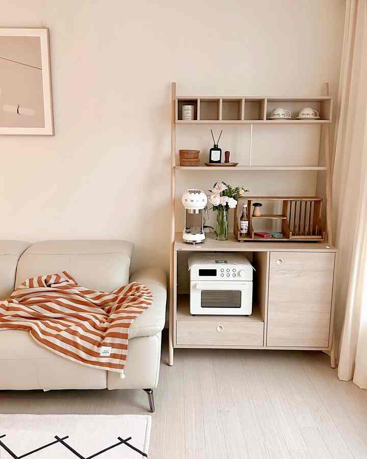 明るいベージュ色調のリビング、白いレザーソファと木製のカフェ風収納が配された雰囲気のある空間