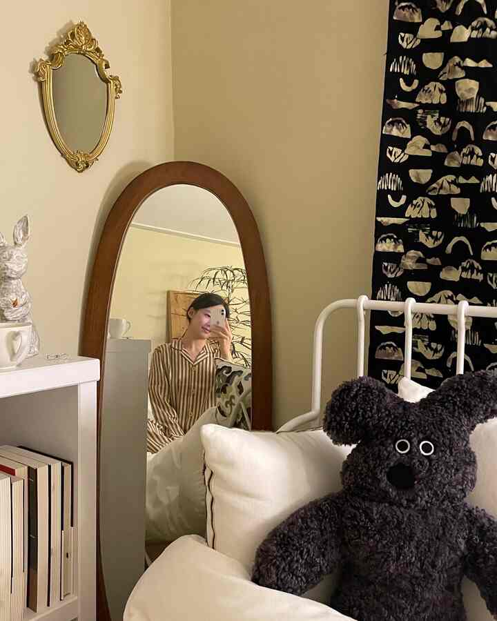 アイボリーとブラウンのトーンの寝室、木製の全身鏡と白いベッド、本棚が配置された雰囲気のあるインテリア