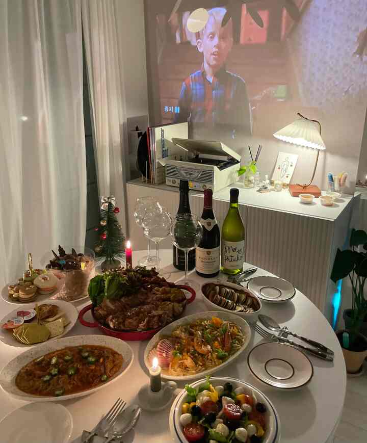 白を基調としたリビングスペース、丸いダイニングテーブルに料理やワイン、キャンドルが配置され、雰囲気のあるホームパーティー空間