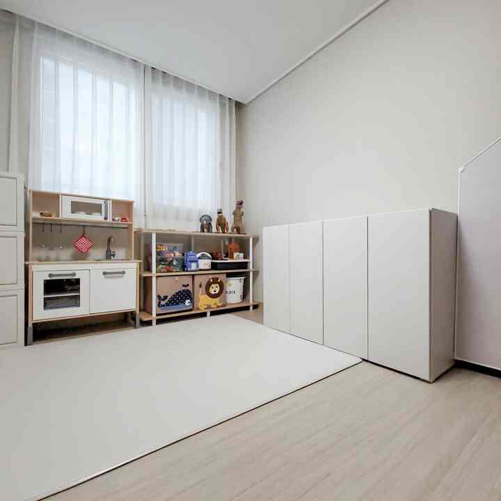 ホワイトとナチュラルカラーの子供部屋、整理されたおもちゃ収納と広いプレイマットがある印象的な空間