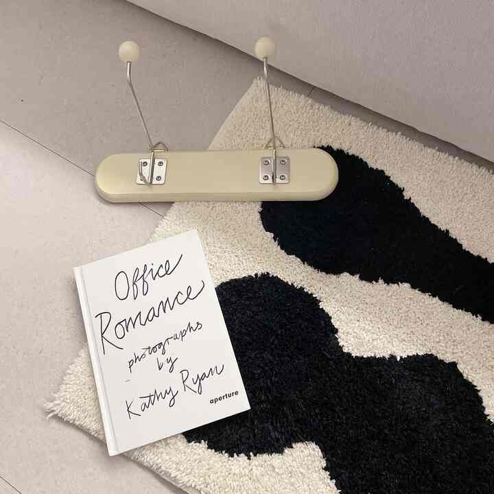 アイボリーと黒の模様がある厚手のマットに手書き文字の白い本とアイボリー色の壁が調和した暖かみのある空間