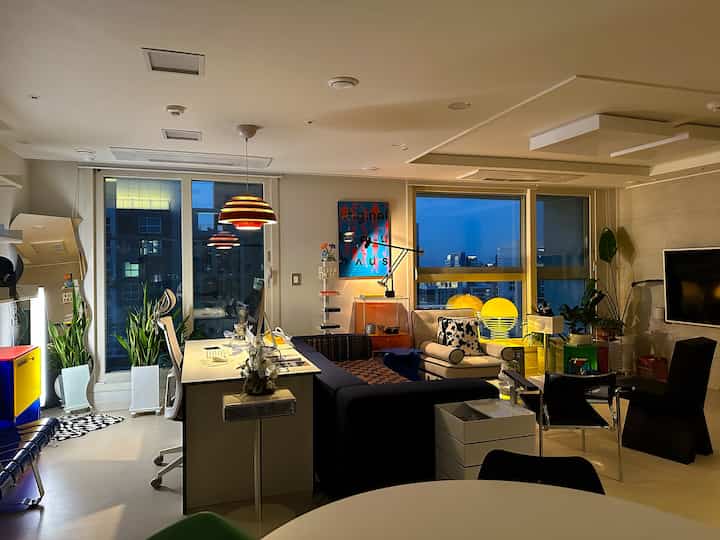 Modern home office and living room featuring white and yellow lighting, desk, and armchair in a stylish interior