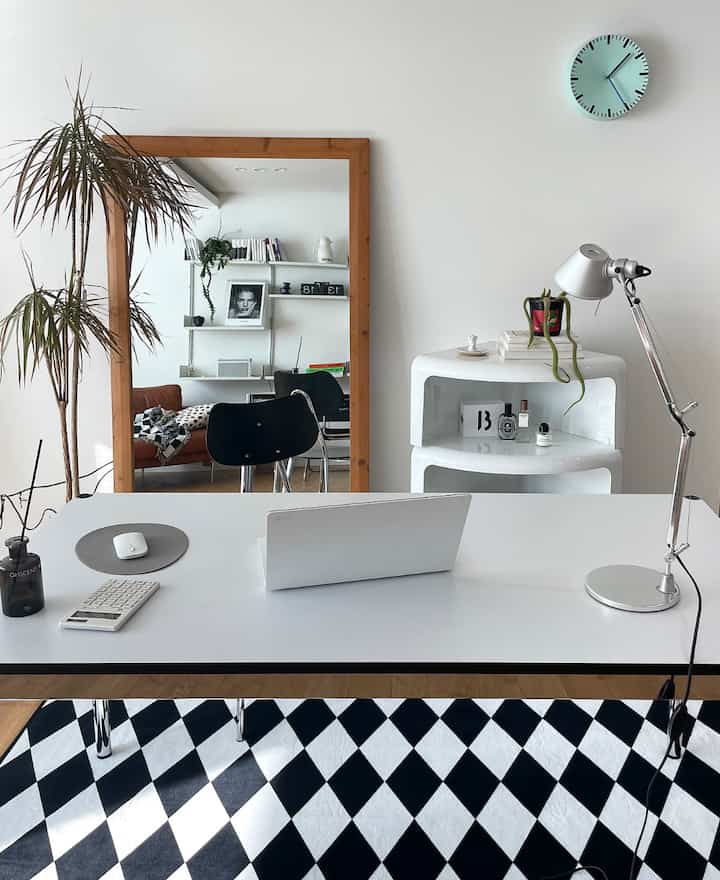 ホワイトとウッドトーンのワークスペース、大きな鏡とモダンなデスク、オフィスチェアが配置された清潔感のあるホームオフィスのインテリア