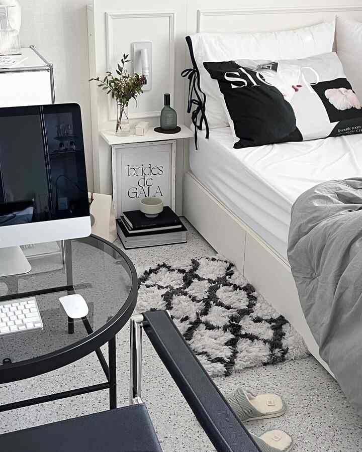 Modern bedroom in white and black tones featuring bed, round glass desk, and patterned shaggy rug creating cozy atmosphere