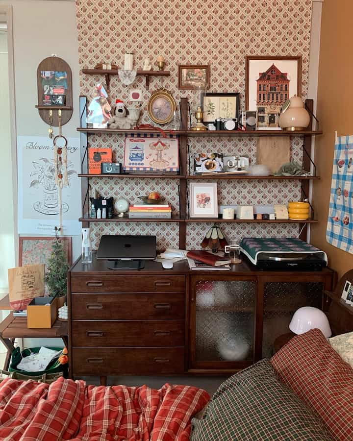 ヴィンテージの木製家具と壁棚にクリスマスの飾りやアートワークが配置されたコンパクトな寝室