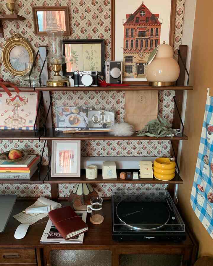 ダークブラウンの木製本棚とヴィンテージ柄の壁紙が調和する小さなワンルーム、様々なヴィンテージの装飾品が配置された雰囲気のあるインテリア