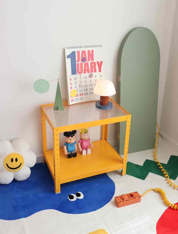 黄色いテーブルと緑の鏡がある子供部屋、キャラクター人形とかわいいモビールが配置された雰囲気のある空間