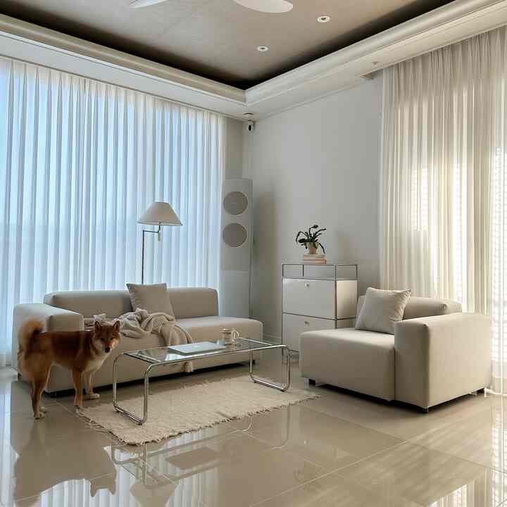 A natural modern living room in white and beige tones featuring beige modular sofas, a glass coffee table, and a floor lamp near the window
