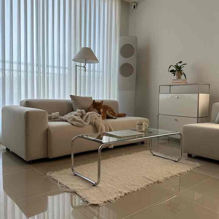 白とナチュラルトーンのリビング、ベージュのソファとガラスのコーヒーテーブル、フロアランプが配置されたシンプルモダンな空間