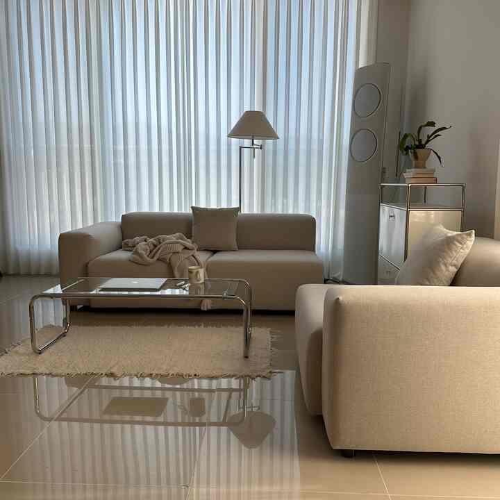 Beige and white toned living room featuring modern beige sofas and a transparent glass coffee table with a warm, clean atmosphere