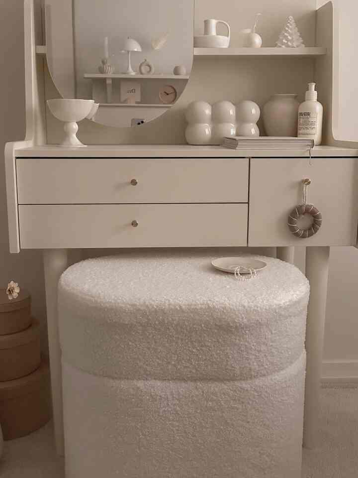 Beige and white toned vanity with round mirror and soft textured white stool, creating a simple and natural space