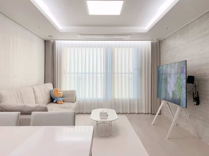 Beige and white tone living room featuring a beige fabric sofa, TV stand, and oval coffee table in a simple setting