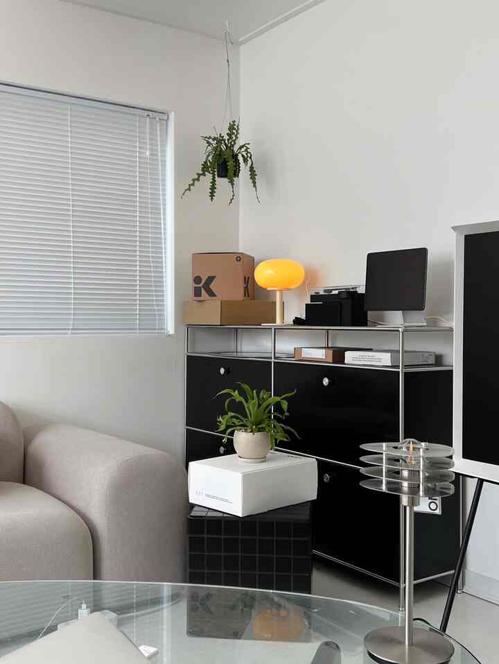 Modern living room with white walls and blinds, featuring a black modular storage cabinet and sofa, creating a clean atmosphere