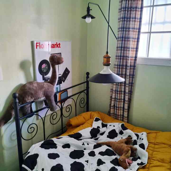 Light green-walled bedroom with black metal bed, yellow bedding and dinosaur plush toys creating a cozy child's space